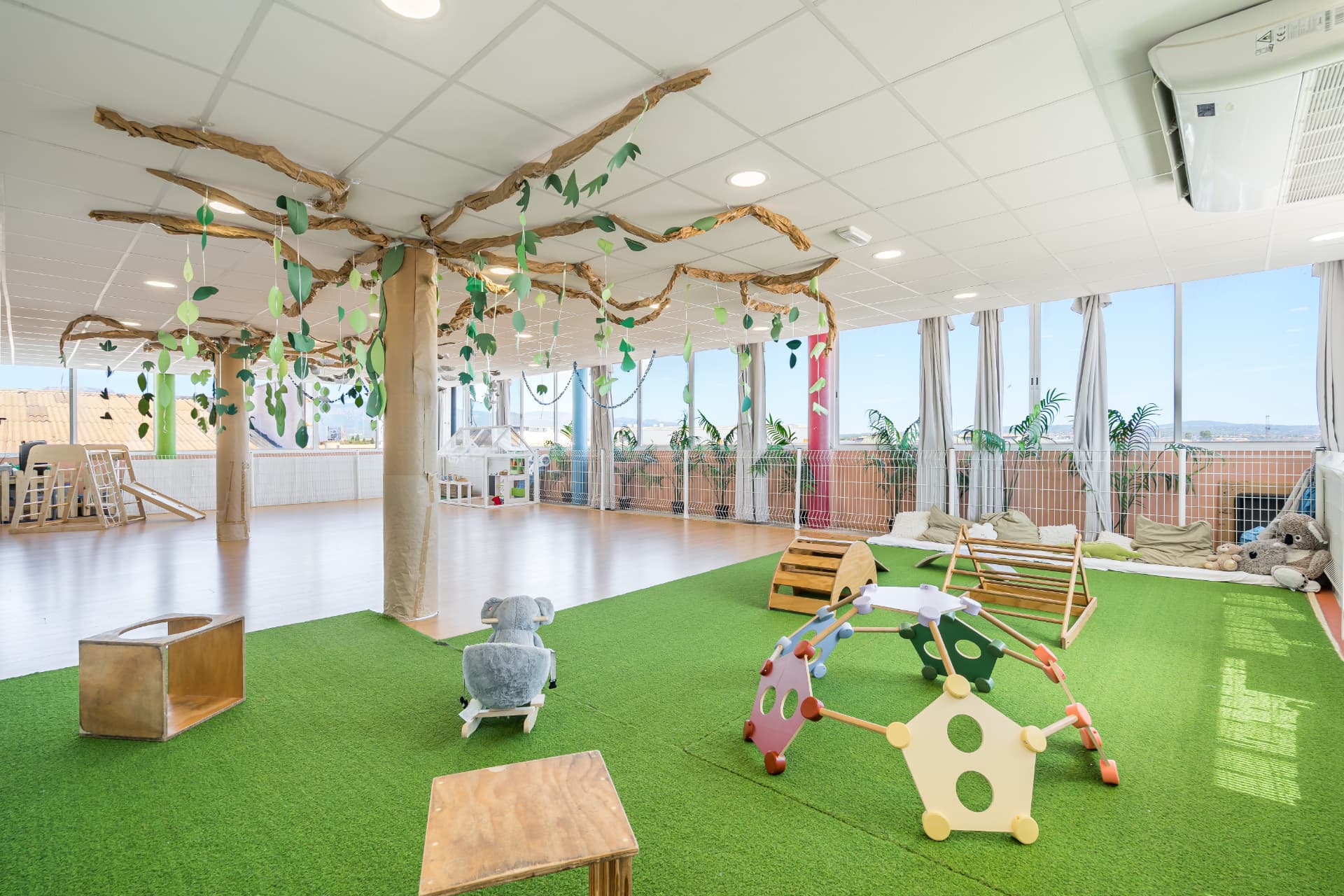 Sala de psicomotricidad con césped artificial, estructuras de madera y columnas decoradas como árboles
